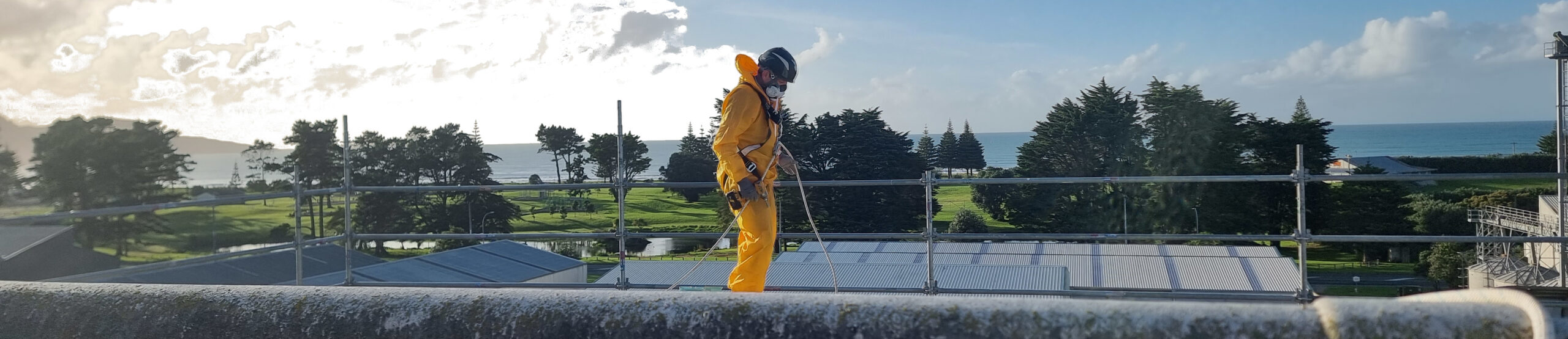 Hazard Pro Team member in safety gear and harnessed on top of a commercial Super6 roof overlooking Gisborne bay.