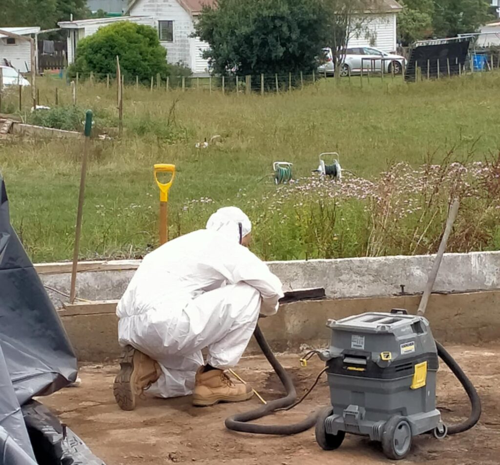 Hazard Pro asbestos removal professional in full protective gear conducting soil remediation at a contaminated site in New Zealand.