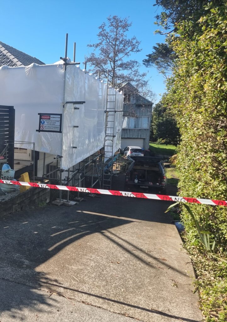 Driveway view of residential house fully shrink‑wrapped after asbestos removal and environmental cleaning by Hazard Pro specialists.