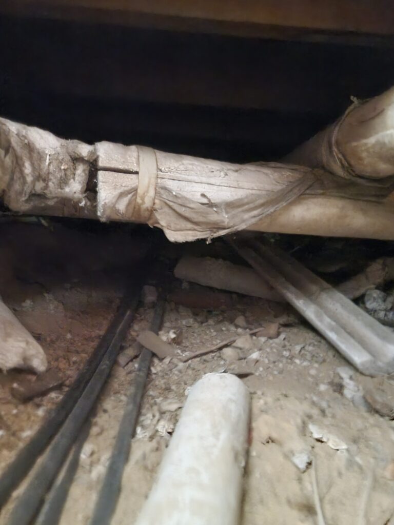 Subfloor area showing asbestos debris and asbestos‑wrapped pipe identified for safe removal by Hazard Pro asbestos specialists.