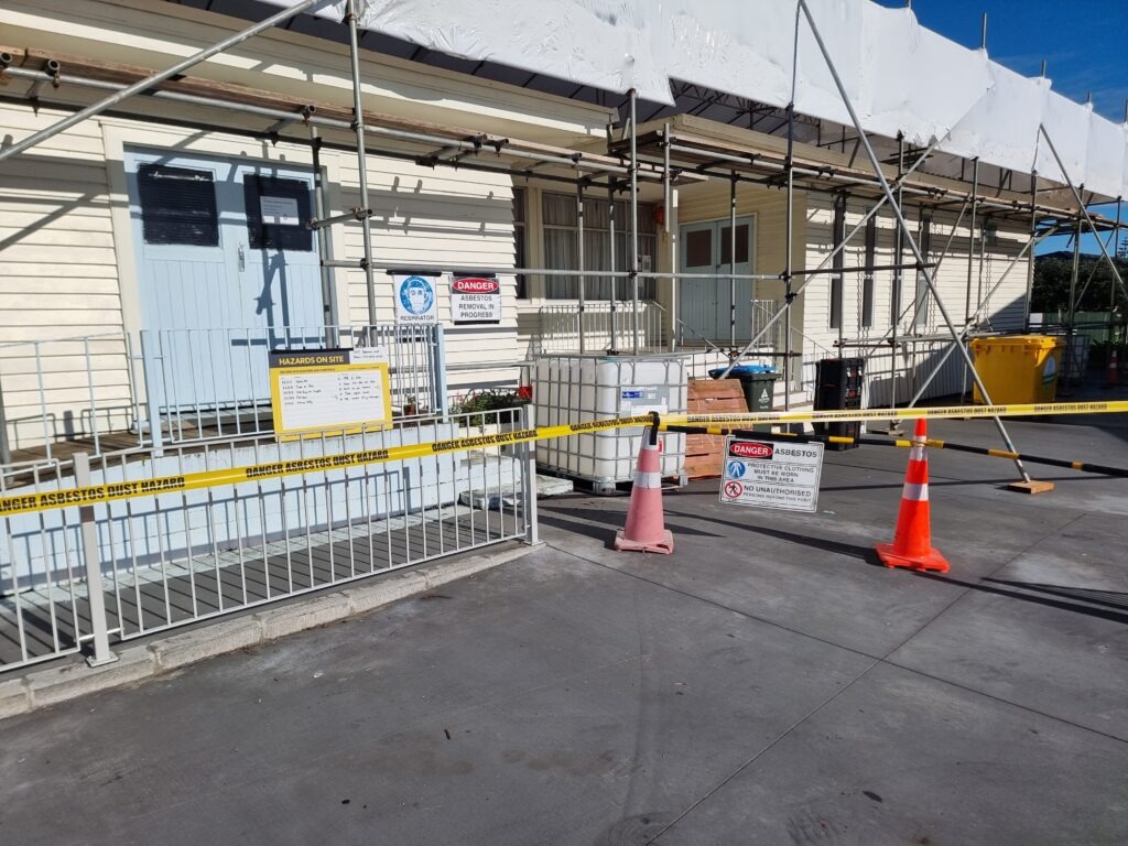 School building in New Zealand undergoing safe asbestos removal by Hazard Pro, with scaffolding, containment barriers, and safety signage in place.