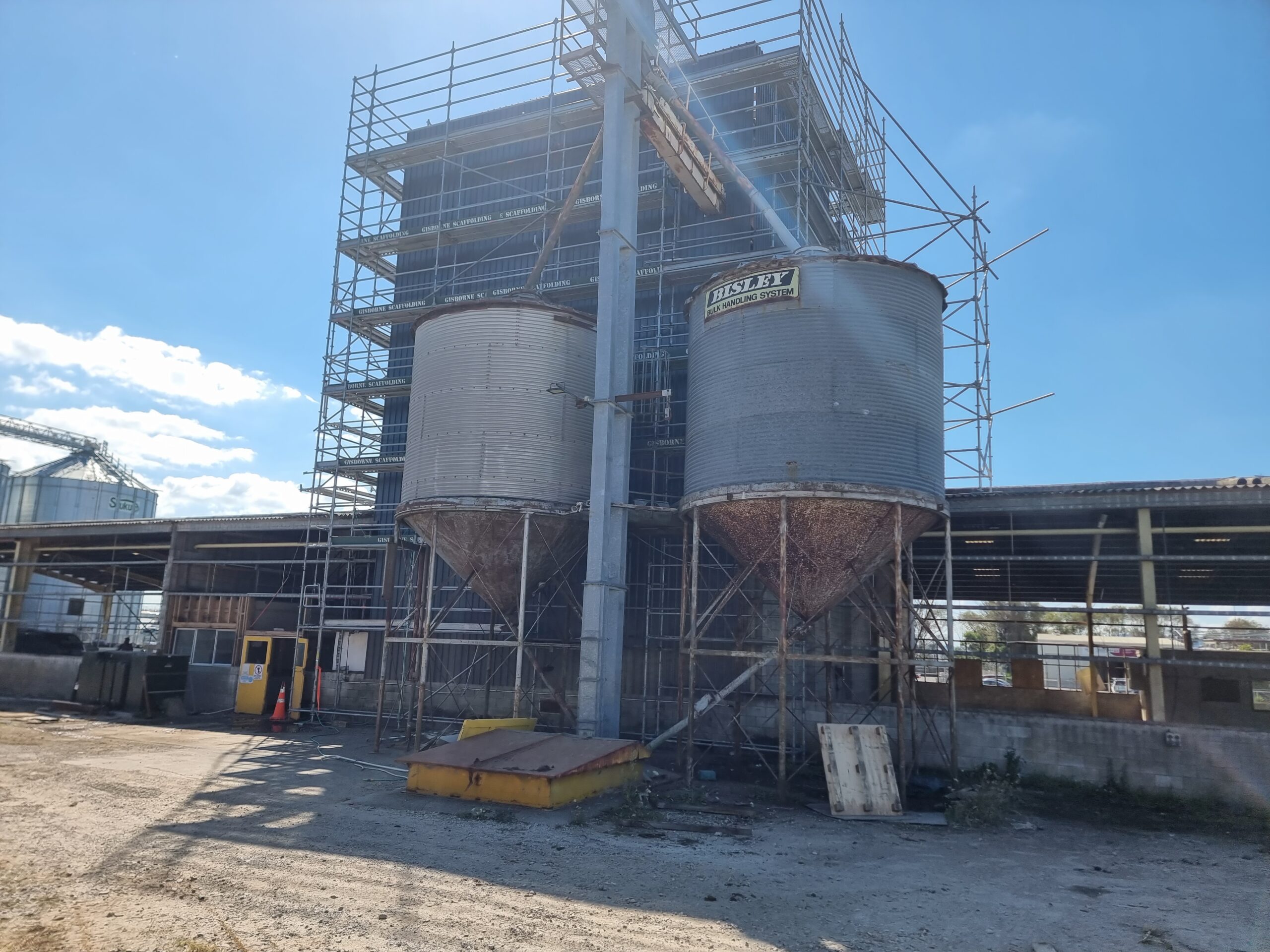 Commercial grain warehouse tower with scaffolding around asbestos cladding on walls and roof made of super6 asbestos roofing material. Prior to asbestos removal.