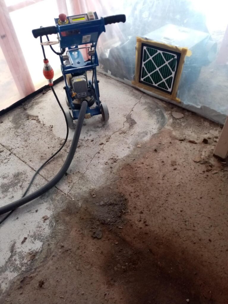 Concrete floor after vinyl lift with grinder in use, mid‑process of removing asbestos mastic by Hazard Pro asbestos removal specialists.
